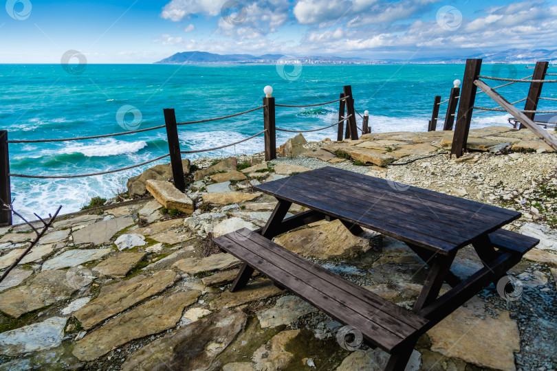 Скачать Курорт Кабардинка. Стол и скамейки стоят на смотровой площадке с видом на штормящее море и город Новороссийск. фотосток Ozero