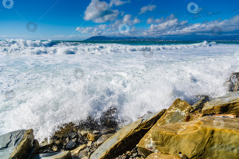 Скачать Курорт Кабардинка. Большие зеленые штормовые волны в белой пене накатываются на каменистый пляж Кабардинки. На заднем плане - порт Новороссийск и Кавказские горы. Большие камни на берегу. Брызги и пена от волн фотосток Ozero