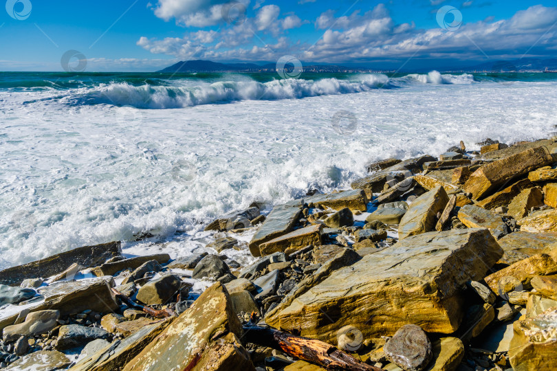 Скачать Курорт Кабардинка. Большие зеленые штормовые волны в белой пене накатываются на каменистый пляж Кабардинки. На заднем плане - порт Новороссийск и Кавказские горы. Большие камни на берегу фотосток Ozero