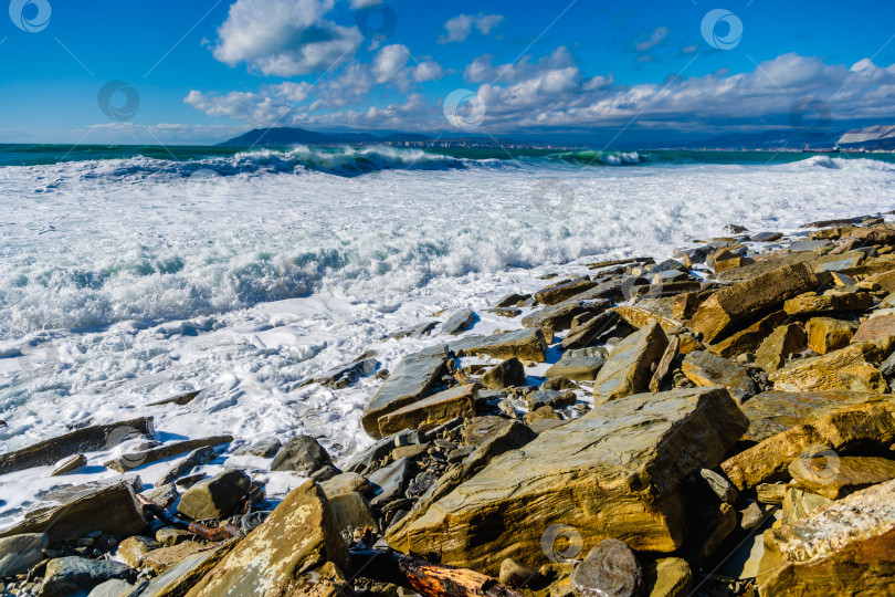 Скачать Курорт Кабардинка. Большие зеленые штормовые волны в белой пене накатываются на каменистый пляж Кабардинки. На заднем плане - порт Новороссийск и Кавказские горы. Большие камни на берегу фотосток Ozero