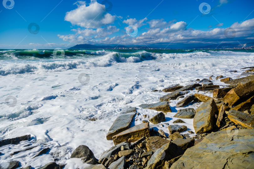 Скачать Курорт Кабардинка. Большие зеленые штормовые волны в белой пене накатываются на каменистый пляж Кабардинки. На заднем плане - порт Новороссийск и Кавказские горы. Большие камни на берегу фотосток Ozero