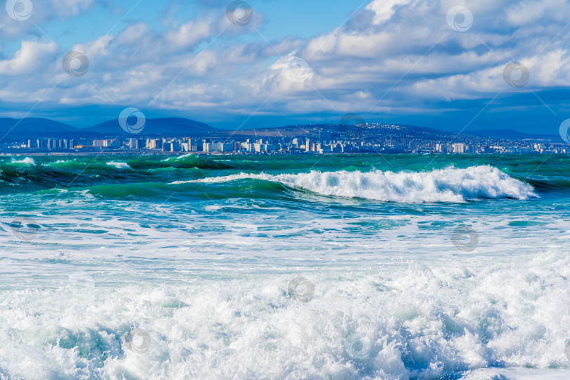 Скачать Курорт Кабардинка. Черное море. Большие штормовые волны изумрудного цвета накатывают на берег. Множество брызг и пены. Порт Новороссийск и Кавказские горы на горизонте фотосток Ozero
