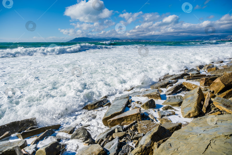 Скачать Курорт Кабардинка. Большие зеленые штормовые волны в белой пене накатываются на каменистый пляж Кабардинки. На заднем плане - порт Новороссийск и Кавказские горы. Большие камни на берегу фотосток Ozero