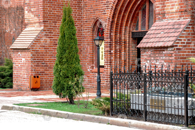 Скачать Историческая церковь из красного кирпича с железной оградой и зеленью фотосток Ozero
