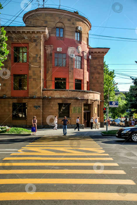 Скачать Городская сцена с историческим зданием и пешеходами на пешеходном переходе в солнечном городе фотосток Ozero