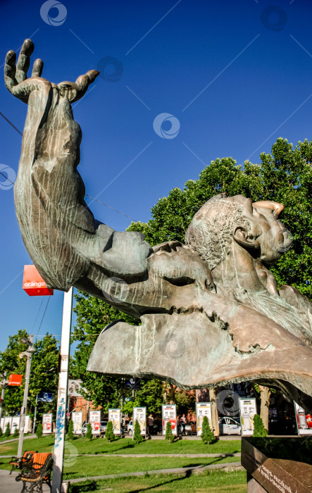 Скачать Динамичная бронзовая скульптура мужской фигуры, устремленной ввысь, в городском парке с голубым небом фотосток Ozero