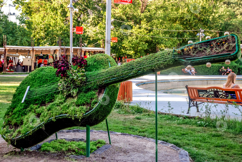 Скачать Пышный топиарий в форме гитары в парке, рядом с которым отдыхают люди фотосток Ozero