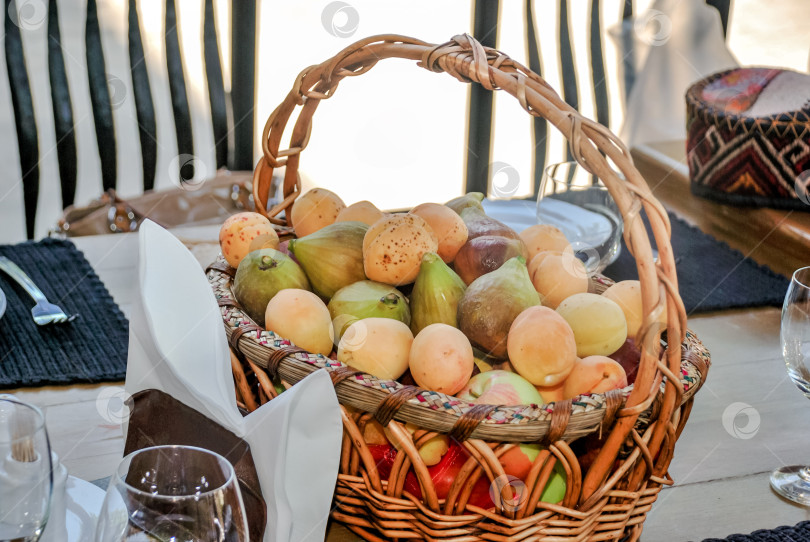 Скачать Корзина свежих фруктов на обеденном столе с салфетками и бокалами фотосток Ozero