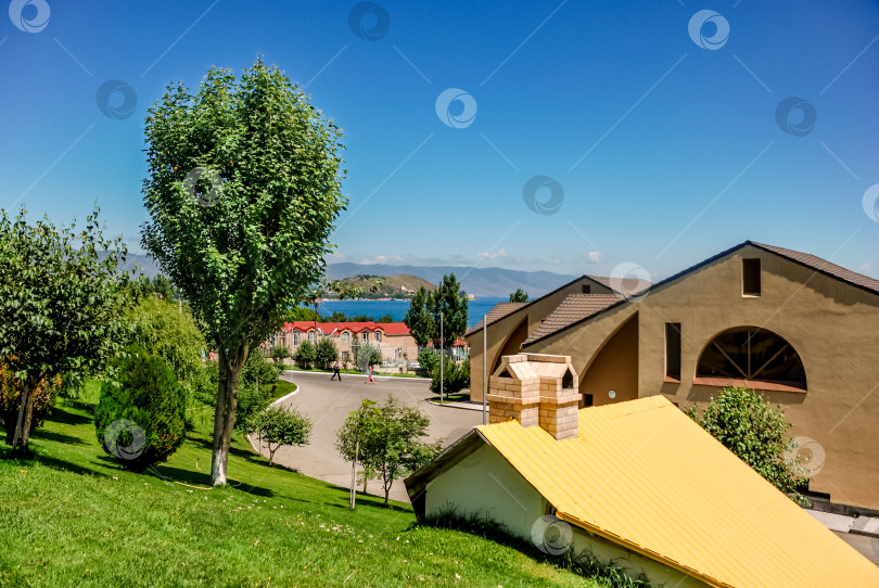 Скачать Солнечный пригородный пейзаж с домами, деревьями и видом на горное озеро фотосток Ozero