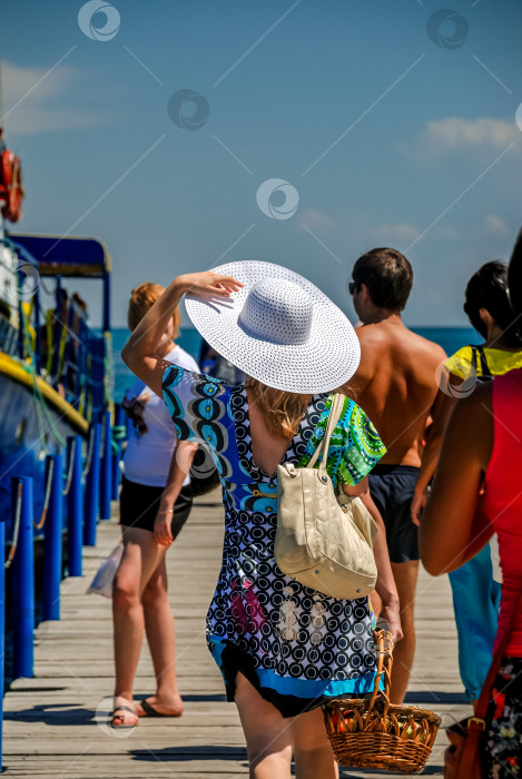 Скачать Туристка в ярком платье и белой шляпе прогуливается по залитому солнцем променаду фотосток Ozero