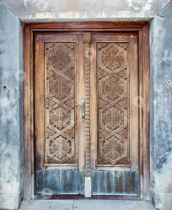 Скачать Деревянная дверь с замысловатой резьбой и геометрическими узорами в выветренной раме фотосток Ozero