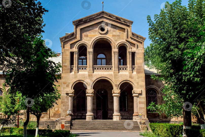 Скачать Историческое каменное здание с арочными окнами и колоннами, окруженное пышной зеленью фотосток Ozero