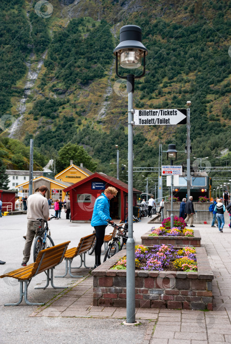 Скачать Живописная сцена железнодорожного вокзала с людьми, велосипедами и яркими цветами в горной деревне фотосток Ozero