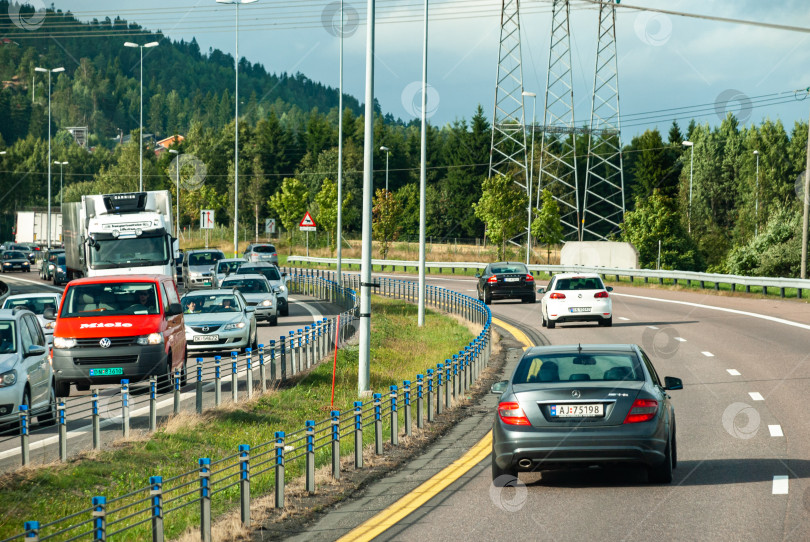 Скачать Оживленное шоссе с легковыми и грузовыми автомобилями, окруженное пышным зеленым лесом фотосток Ozero