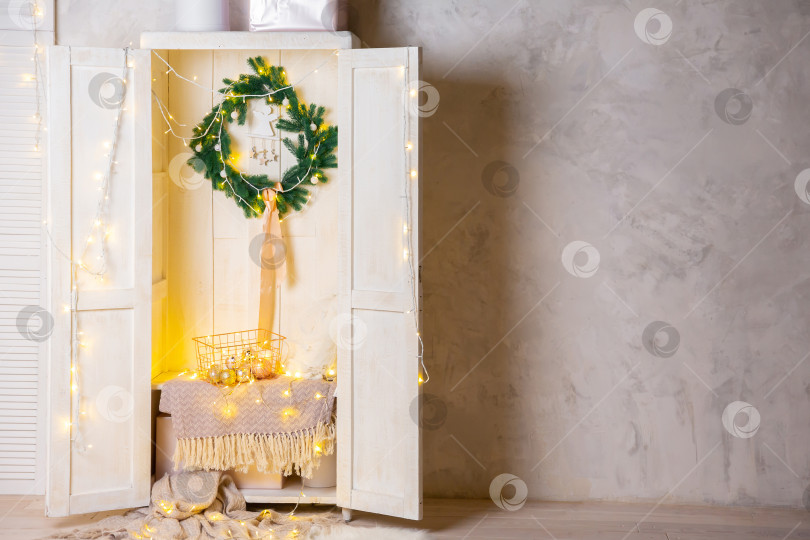 Скачать Корзина из золотистого металла на полке в белом деревянном шкафу или гардеробе. Гирлянды, новогодние игрушки и шары в корзине фотосток Ozero