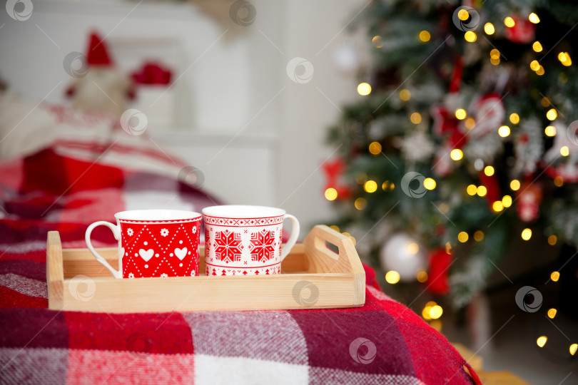 Скачать Кружки на деревянном подносе возле рождественской елки. Концепция уютного домашнего вечера фотосток Ozero