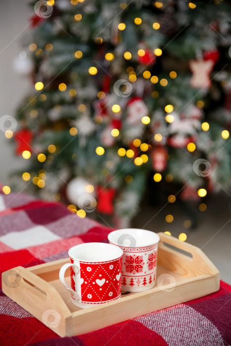 Скачать Кружки на деревянном подносе возле рождественской елки. Концепция уютного домашнего вечера фотосток Ozero