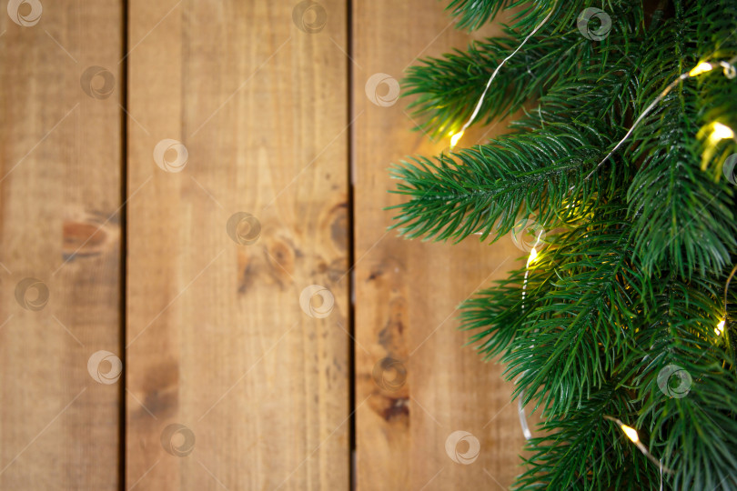 Скачать Зеленые еловые ветки с гирляндой на грубых деревянных досках. фотосток Ozero