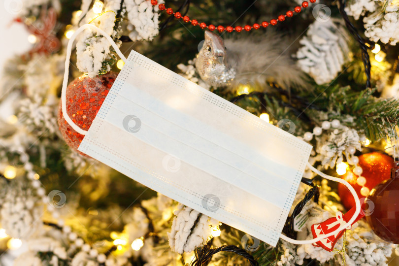 Скачать медицинская маска для лица, висящая на украшенной рождественской елке фотосток Ozero