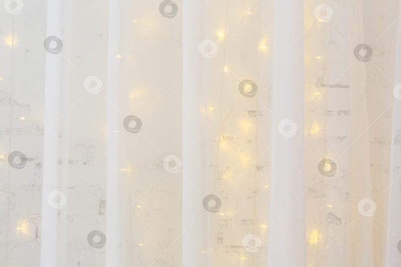 Скачать Новогодний, рождественский фон. Белая тюлевая занавеска на фоне белой кирпичной стены, украшенной горящей гирляндой фотосток Ozero