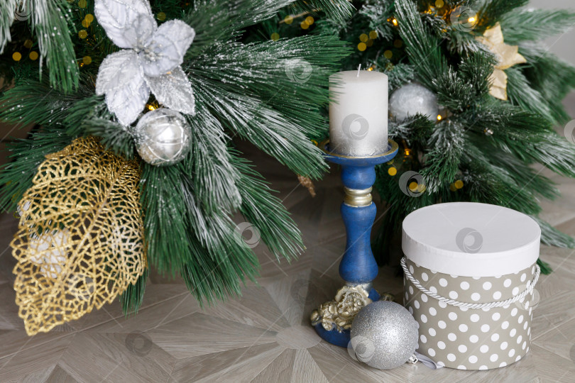 Скачать Рождественская открытка. Подсвечник с белой свечой. Подарочная коробка под рождественской елкой. Еловые ветки на снегу. фотосток Ozero