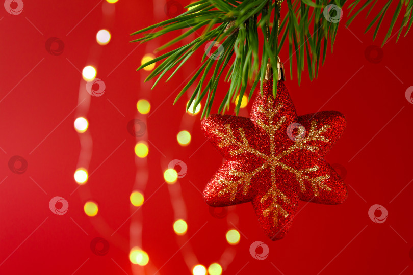 Скачать Новогодняя игрушка, висящая на еловой ветке, на фоне гирлянды фотосток Ozero