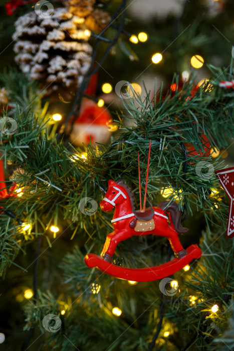 Скачать Игрушечная красная лошадка, висящая на зеленой ветке рождественской елки фотосток Ozero