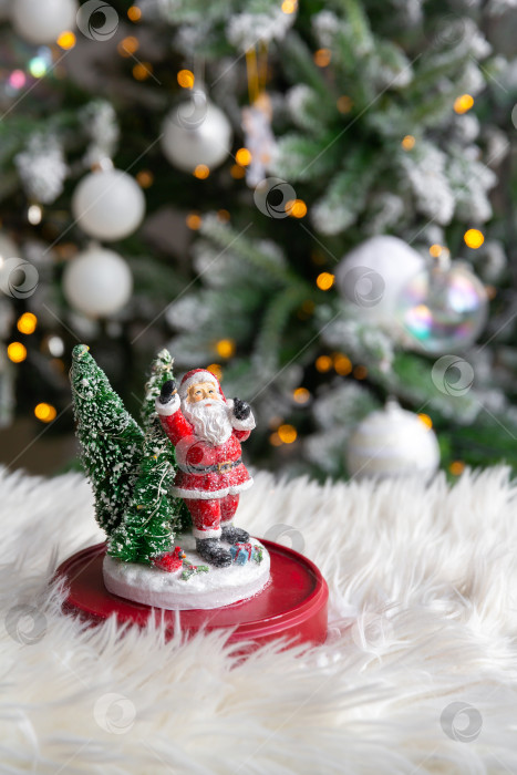 Скачать фигурка Деда Мороза на белом меховом одеяле, на фоне горящей гирлянды рождественской елки. фотосток Ozero