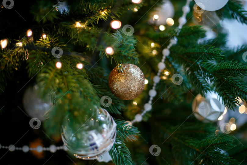 Скачать Зеленые рождественские веточки, украшенные белыми и золотистыми шариками, бусинами и гирляндой фотосток Ozero