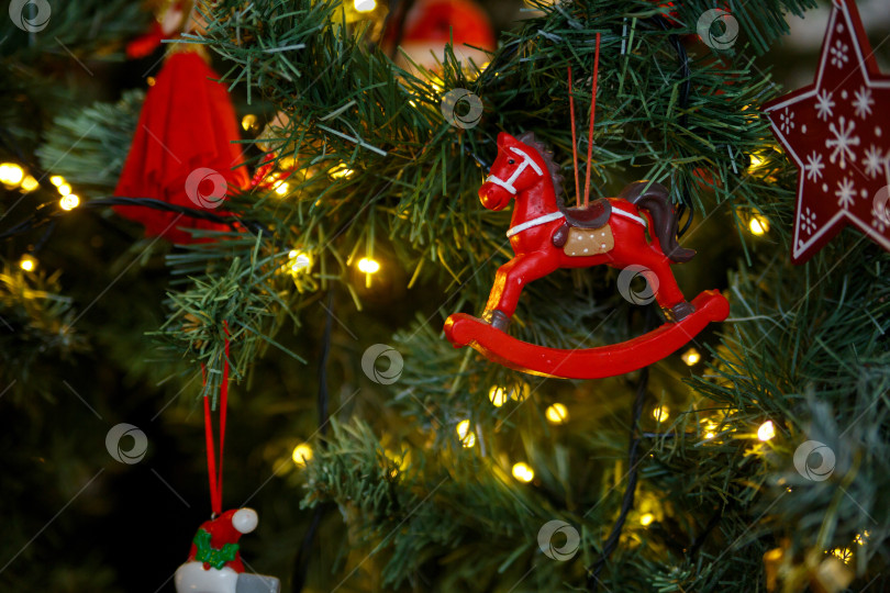 Скачать Игрушечная красная лошадка, висящая на зеленой ветке рождественской елки фотосток Ozero