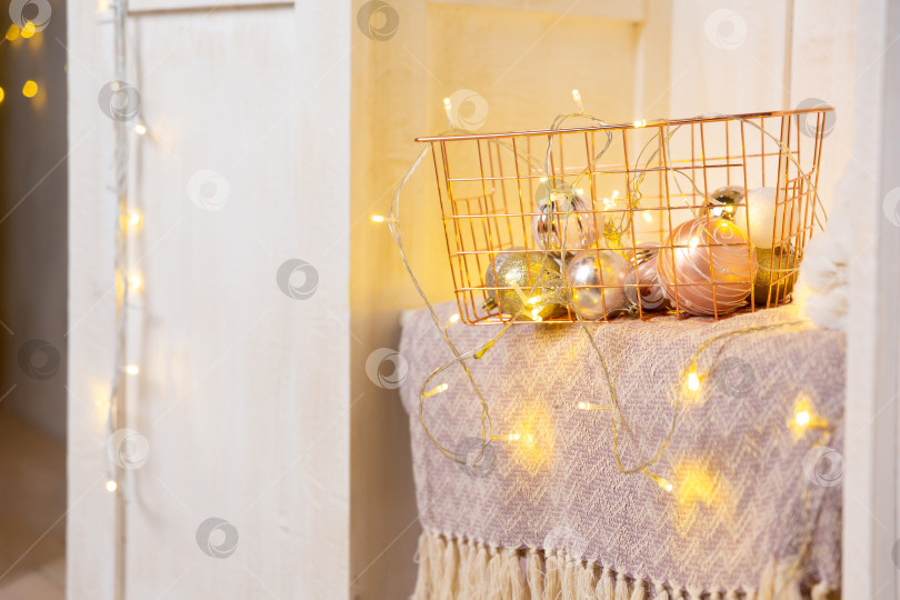Скачать Корзина из золотистого металла на полке в белом деревянном шкафу или гардеробе. Гирлянды, елочные игрушки и шары в корзине фотосток Ozero