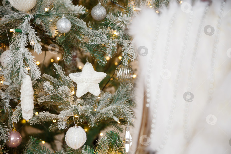 Скачать Белая рождественская игрушка, висящая на зеленой заснеженной еловой ветке фотосток Ozero