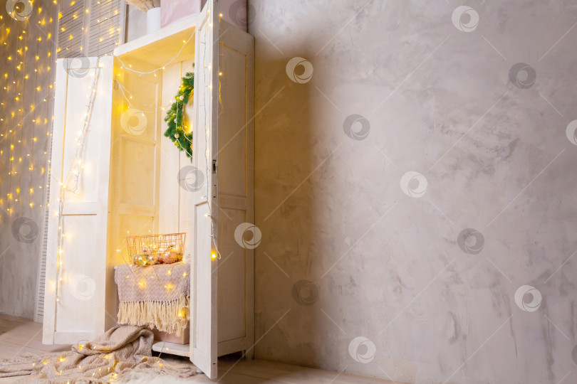 Скачать Корзина из золотистого металла на полке в белом деревянном шкафу или гардеробе. Гирлянды, елочные игрушки и шары в корзине фотосток Ozero