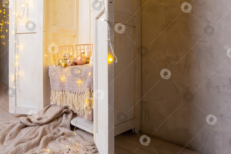 Скачать Корзина из золотистого металла на полке в белом деревянном шкафу или гардеробе. Гирлянды, елочные игрушки и шары в корзине фотосток Ozero