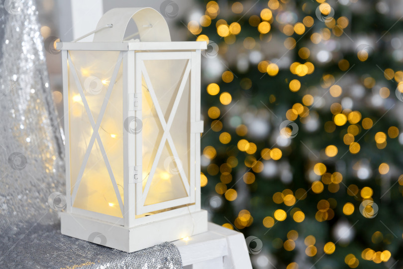 Скачать Белый фонарь стоит на ткани с блестками на фоне гирлянд огней фотосток Ozero