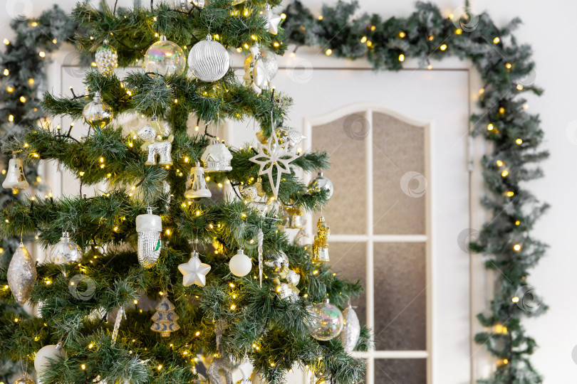 Скачать Поздравительная новогодняя открытка. Рождественская елка, украшенная гирляндой, на фоне двери фотосток Ozero