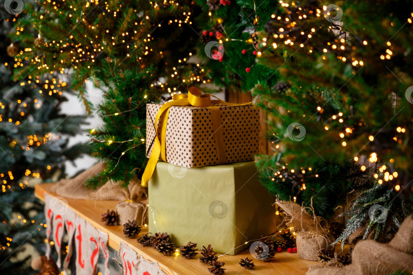 Скачать Подарки в коробках в упаковке стоят возле новогодней елки на деревянном столе фотосток Ozero
