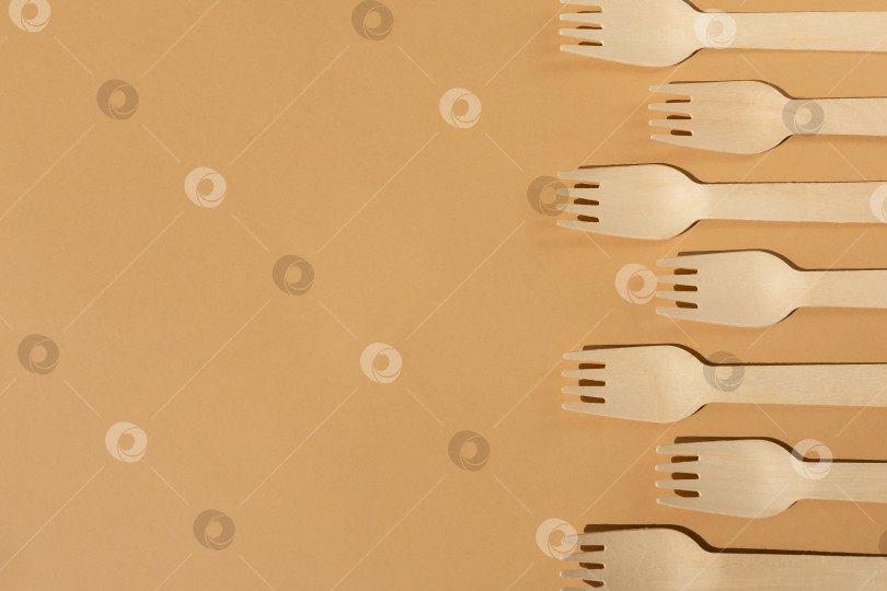 Скачать Деревянные вилки на бежевом, коричневом фоне. Контрастное освещение. Плоская форма. Экологически чистые деревянные столовые приборы. Концепция без использования пластика фотосток Ozero