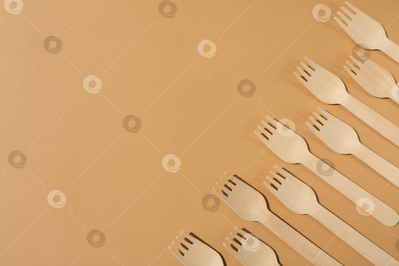 Скачать Деревянные вилки на бежевом или коричневом фоне. Контрастное освещение. Экологически чистые деревянные столовые приборы. Концепция без использования пластика фотосток Ozero