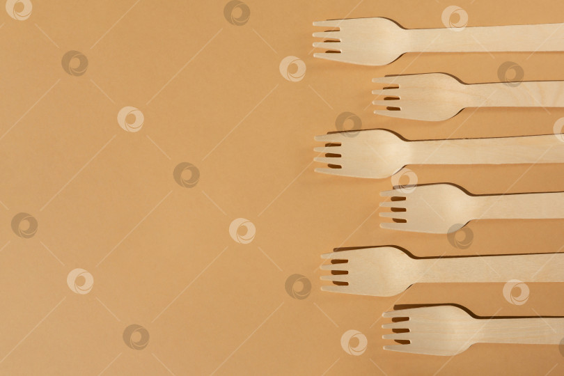 Скачать Деревянные вилки на бежевом, коричневом фоне. Контрастное освещение. Плоская форма. Экологически чистые деревянные столовые приборы. Концепция без использования пластика фотосток Ozero