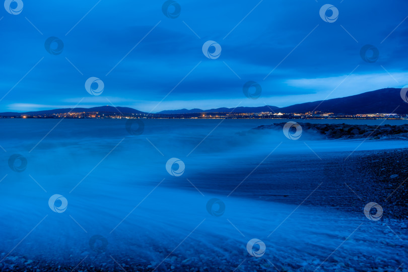 Скачать Шторм в Геленджике при длительной выдержке. Волны в виде тумана набегают на пляж Геленджика. Сумерки, закат солнца. Горы и городские огни на горизонте фотосток Ozero