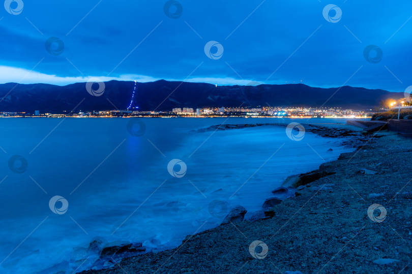 Скачать Шторм в Геленджике при длительной выдержке. Волны в виде тумана набегают на пляж Геленджика. Сумерки, закат солнца. Горы и городские огни на горизонте фотосток Ozero