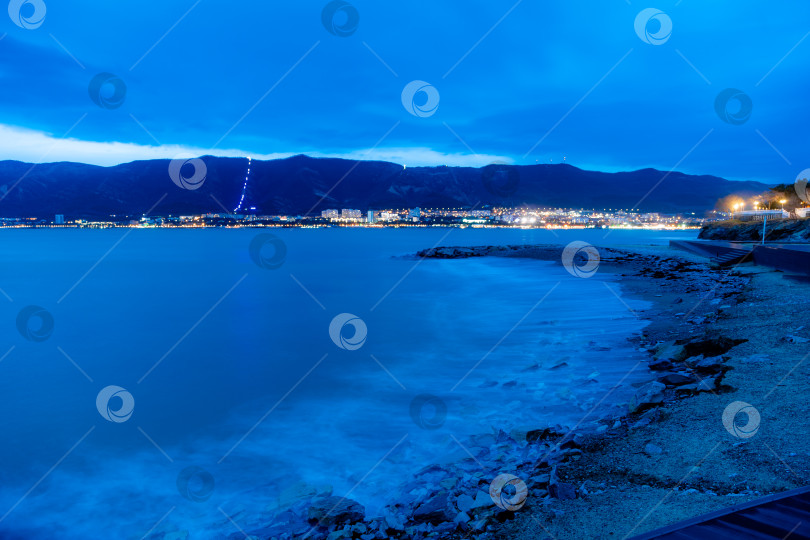 Скачать Шторм в Геленджике на большой дистанции. Волны в виде тумана набегают на пляж Геленджика. Сумерки, закат солнца. Горы и городские огни на горизонте фотосток Ozero