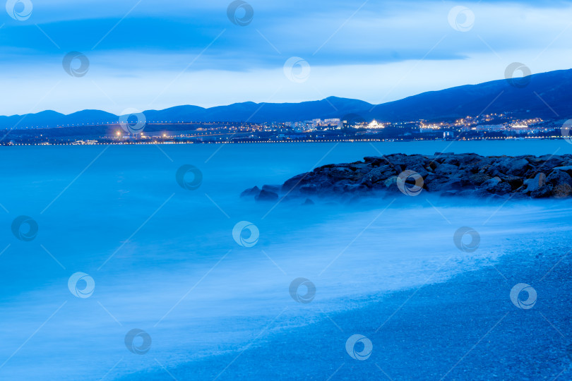 Скачать Шторм в Геленджике при длительной выдержке. Волны в виде тумана набегают на пляж Геленджика. Сумерки, закат солнца. Горы и городские огни на горизонте фотосток Ozero