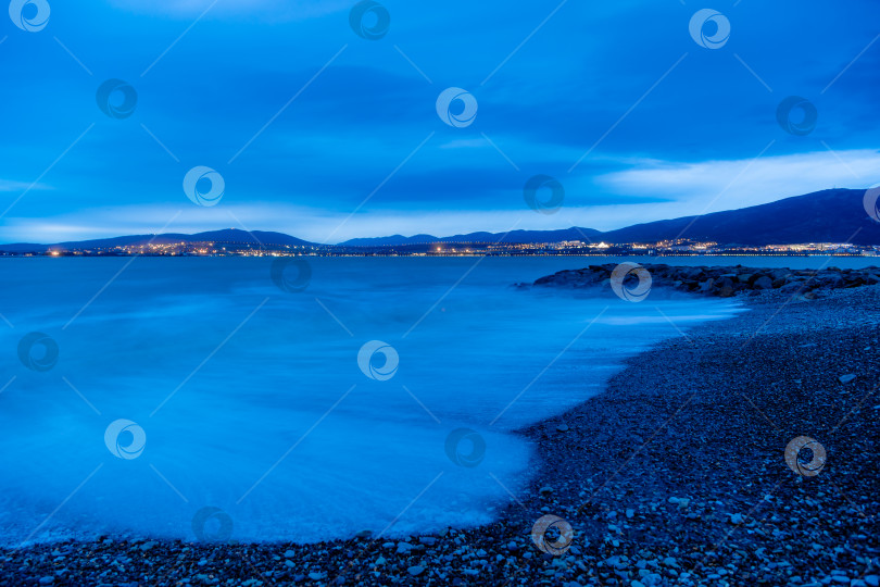 Скачать Шторм в Геленджике на большой дистанции. Волны в виде тумана набегают на пляж Геленджика. Сумерки, закат солнца. Горы и городские огни на горизонте фотосток Ozero