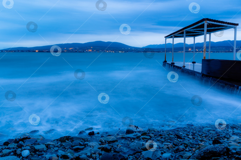 Скачать Шторм в Геленджике на длительной выдержке. Волны в виде тумана набегают на пляж Геленджика. Пирс. Сумерки, закат. Горы и городские огни на горизонте фотосток Ozero