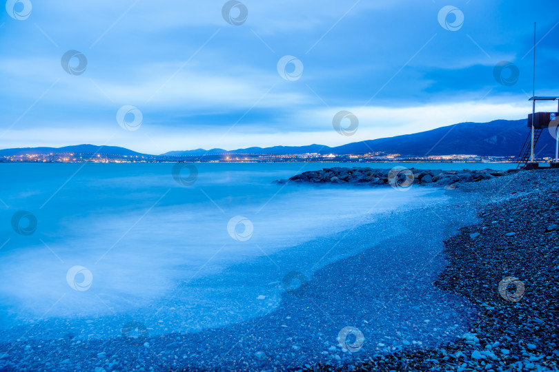 Скачать Шторм в Геленджике на большой дистанции. Волны в виде тумана набегают на пляж Геленджика. Сумерки, закат солнца. Горы и городские огни на горизонте фотосток Ozero