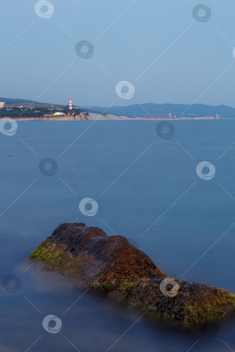 Скачать Геленджикский маяк на закате. Маяк стоит на высоком скалистом берегу. На переднем плане - камень в водорослях фотосток Ozero
