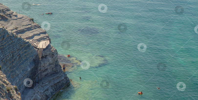 Скачать Геленджик. Пляж Сосновка. Высокая белая скала и пляж у подножия обрыва. Чистое теплое море. Люди будут загорать на пляже. фотосток Ozero