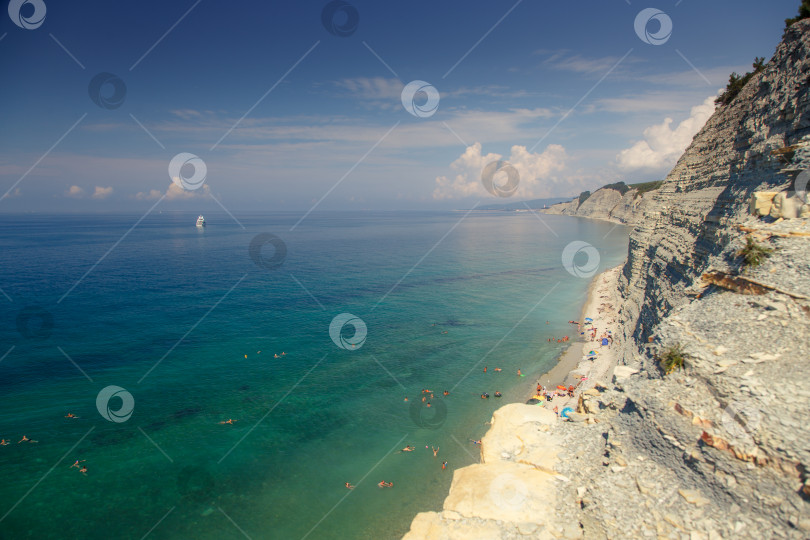 Скачать Большая белая моторная яхта стоит у крутого высокого скалистого берега. На вершине скалы растут сосны. Геленджик, Черное море. Спокойное, гладкое море фотосток Ozero